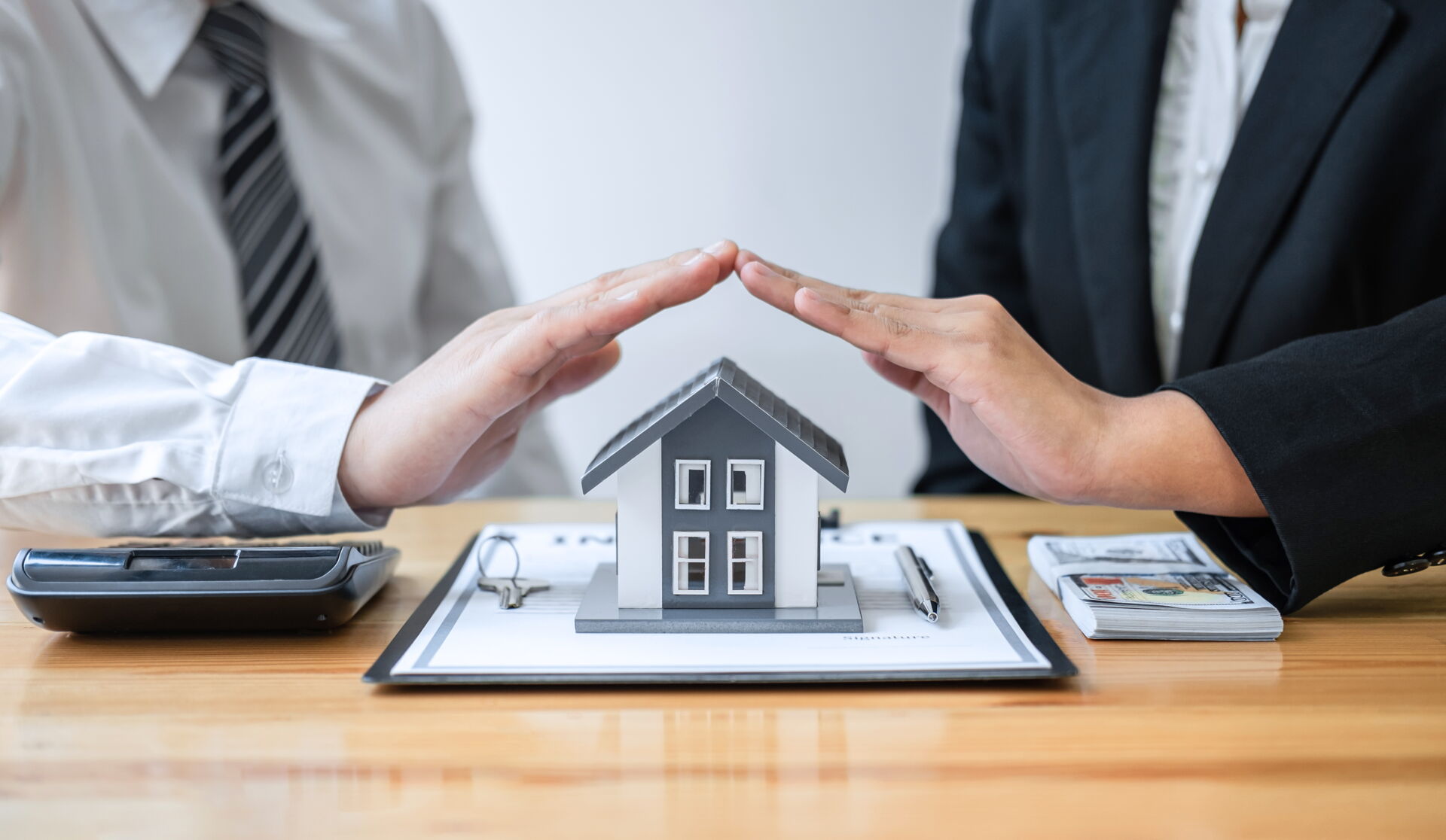 Zwei Hände schützen symbolisch ein Hausmodell über einem Vertrag in Bautzen. Immobilien Anders GmbH – Ihr sicherer Partner für Immobilien.